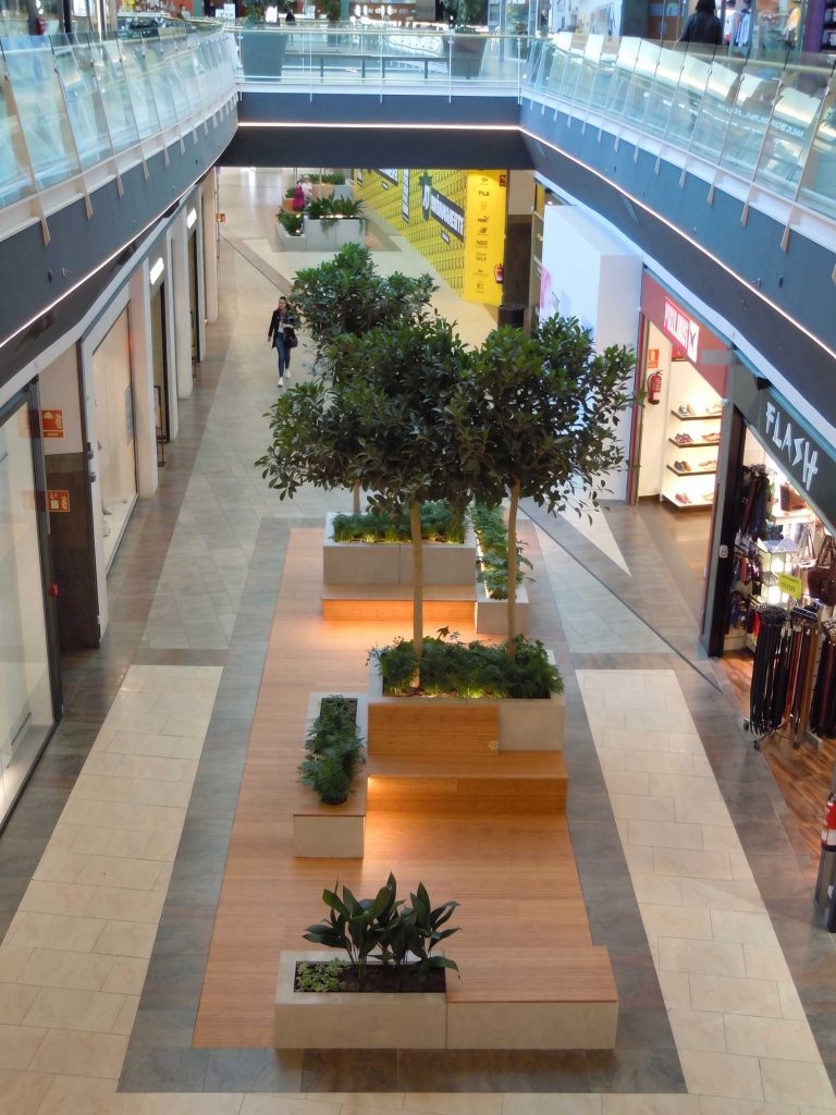 Interior de un centro comercial con áreas verdes y plantas, ideal para reformas y construcciones de espacios modernos.