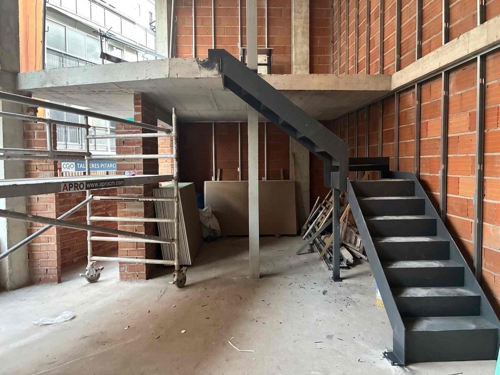 Escalera moderna en construcción con estructura de ladrillos y materiales de reforma en el interior. Apro CM.