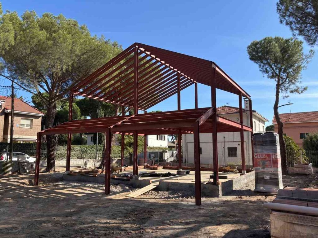 Estructura de acero en construcción para reformas y edificaciones en Apro CM, con árboles y viviendas al fondo.